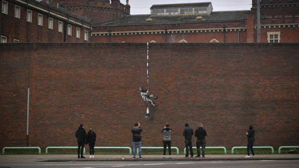 Граффити художника Бэнкси на внешней стене закрытой Редингской тюрьмы, заключенный в тюремной робе, спускающийся по веревке, которая сверху выглядит как связанные простыни, а снизу — как длинный лист бумаги, тянущийся из печатной машинки - Sputnik Азербайджан