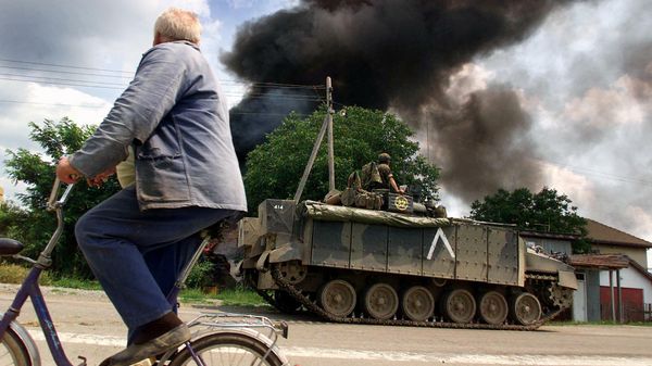 Житель проезжает мимо горящего сербского дома в Косовске-Митровице, 3 июля 1999 года - Sputnik Азербайджан