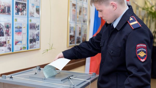 Сотрудник полиции опускает бюллетень в урну на выборах президента РФ на избирательном участке №51 в Петропавловске-Камчатском - Sputnik Азербайджан
