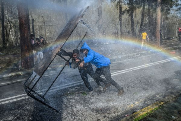 Migrants take cover behind a wooden board as Greek police uses water cannons to block them trying to break fences in the Turkey-Greece border province of Edirne - Sputnik Азербайджан